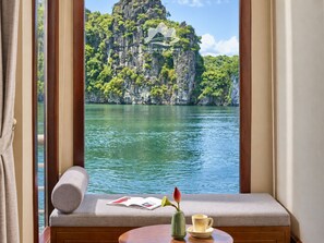 A room with a window overlooking a body of water and a mountainous landscape. - Verdure Lotus Classic Cruise on Lan Ha Bay (Tuan Chau)