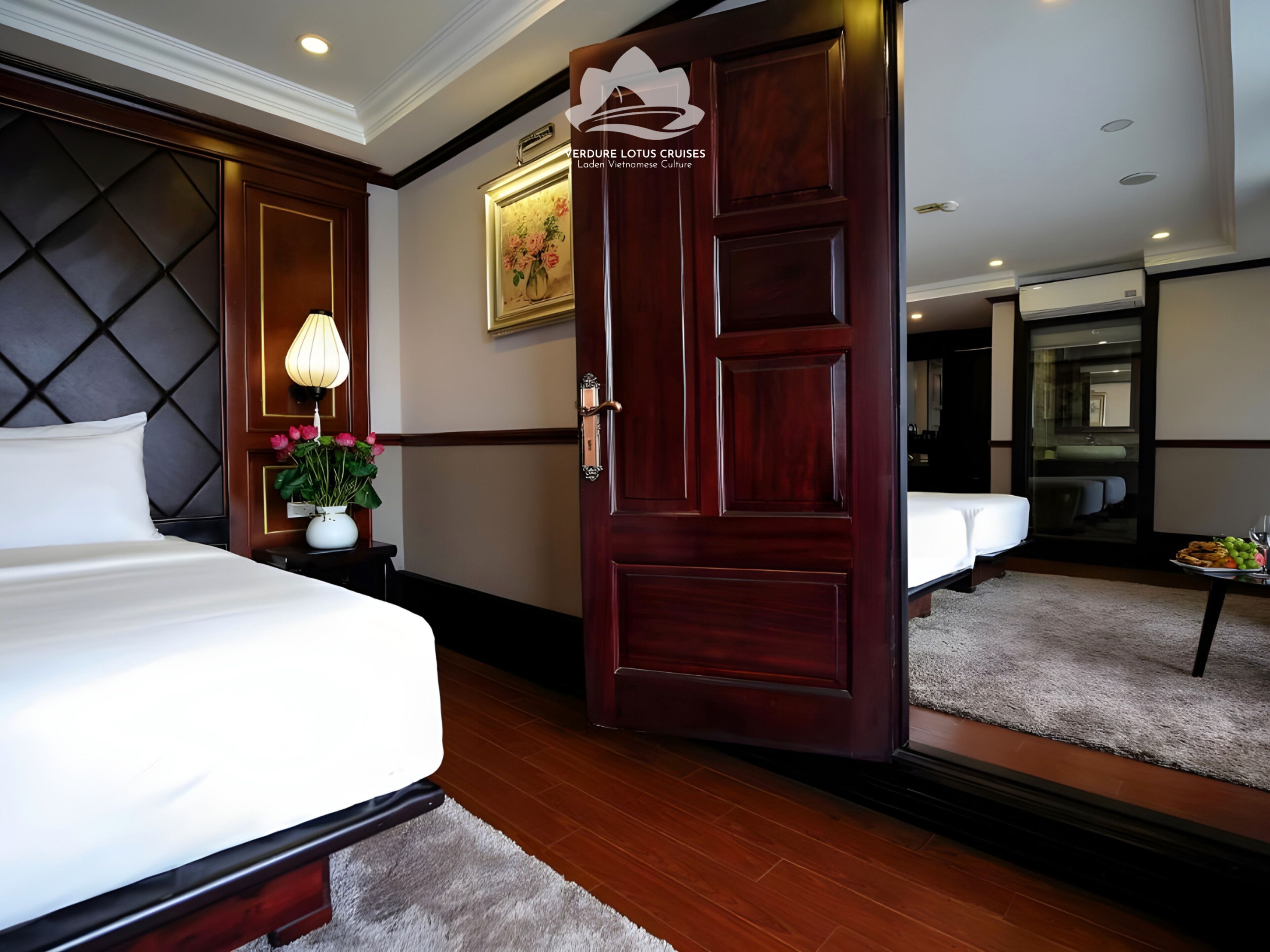 Une chambre d’hôtel avec un lit, une table de chevet avec une lampe et des fleurs, une porte en bois et un miroir.