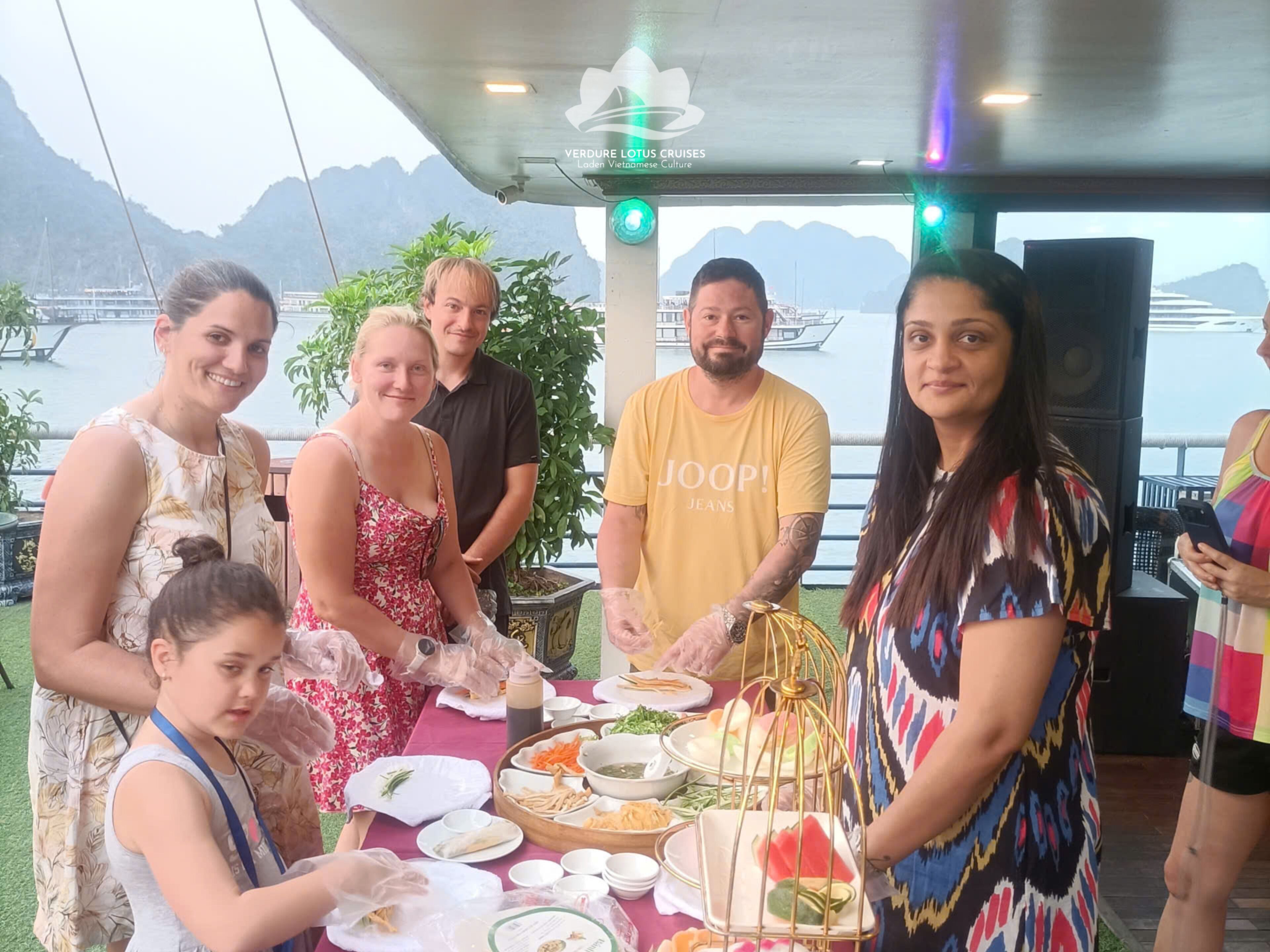 Eine Gruppe von Menschen speist an einem Tisch im Freien mit Blick auf das Meer und die Berge.