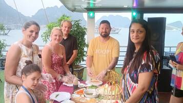 Un grupo de personas cenando en una mesa al aire libre con vistas al mar y a las montañas.