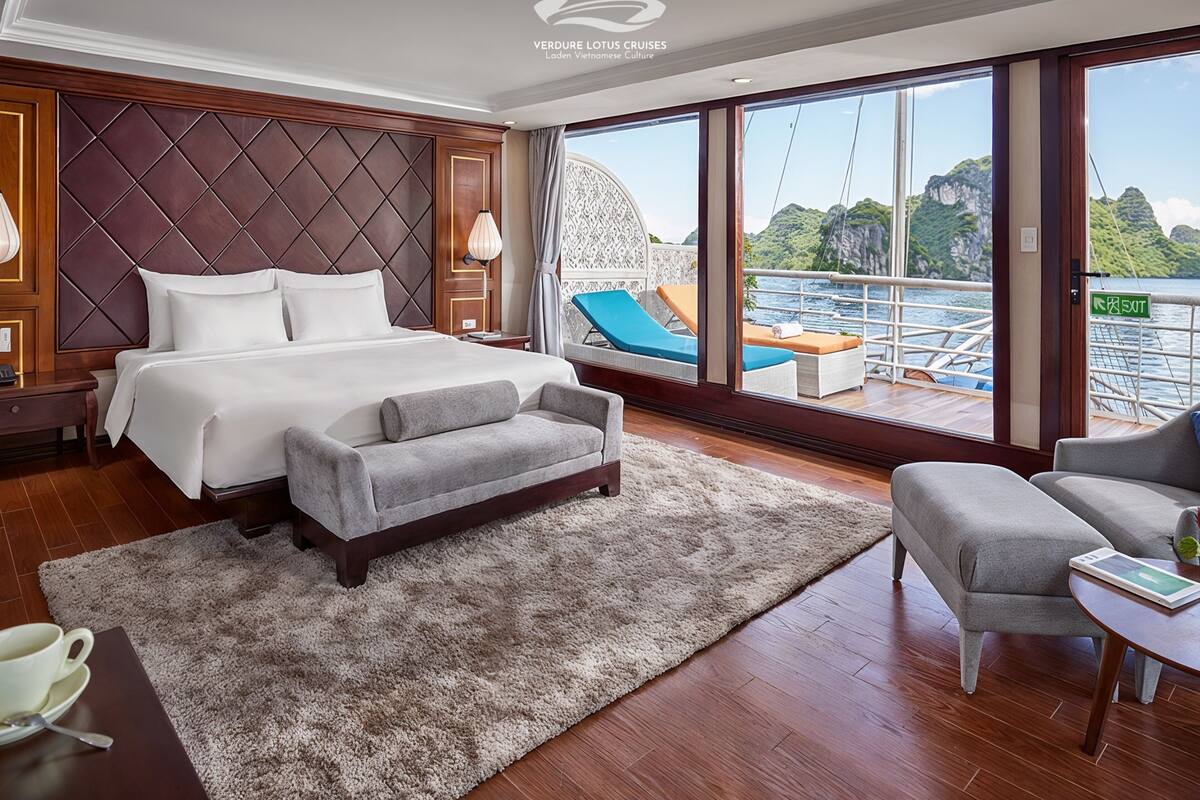 A spacious bedroom with a large bed, a sitting area, and a view of the sea.