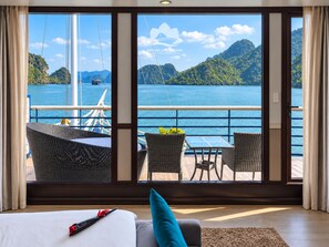 A room with a large window offering a view of a body of water and mountains. - Verdure Lotus Classic Cruise on Lan Ha Bay (Tuan Chau)