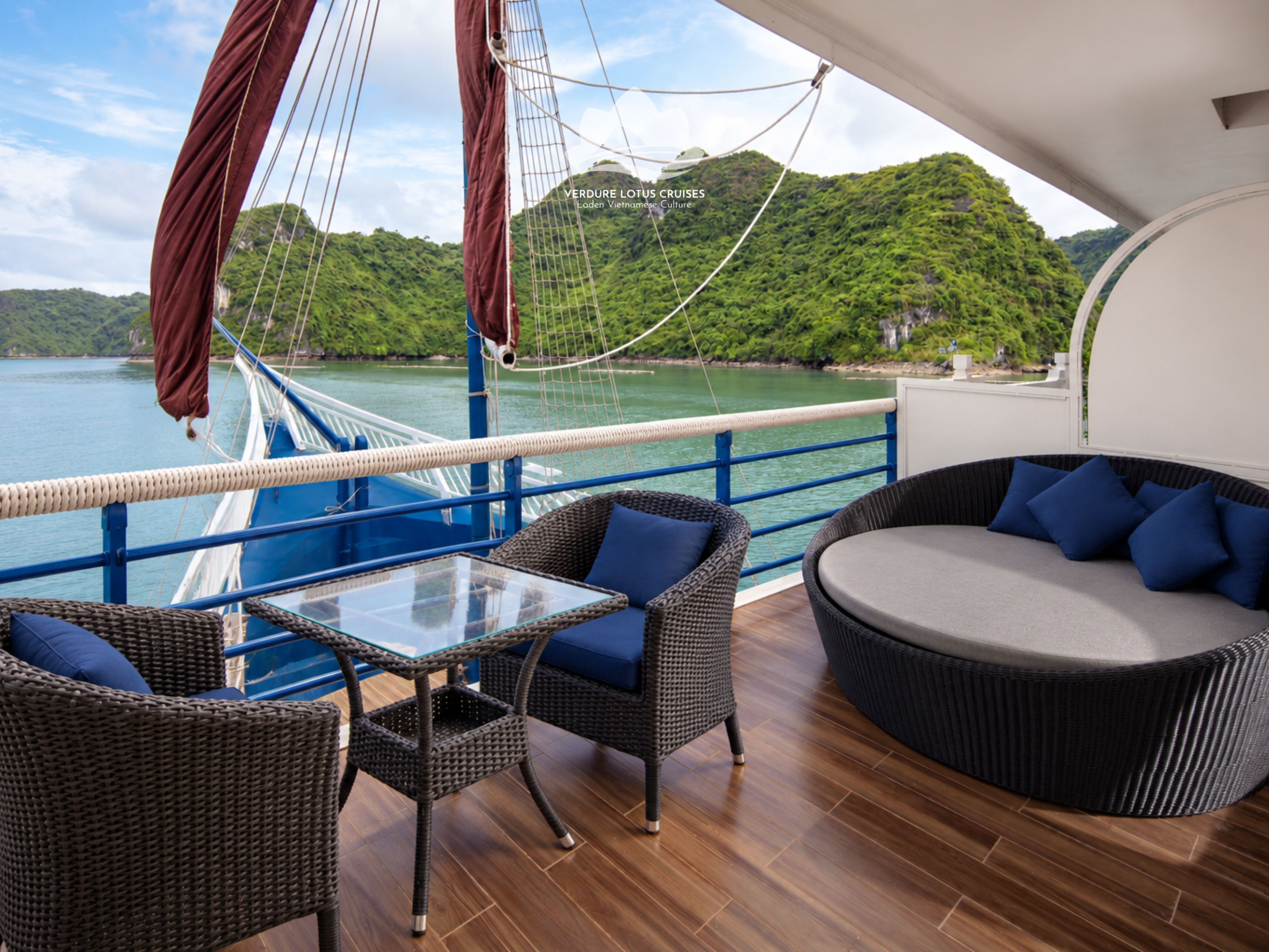 A deck with wicker furniture, a glass table, and a view of a lush green landscape.