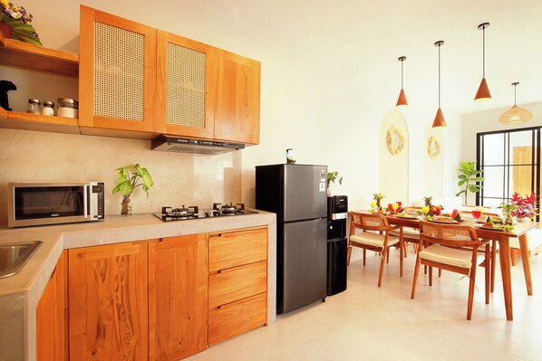Una cocina moderna con armarios de madera, un refrigerador negro, un microondas y un comedor con sillas y una mesa de madera.