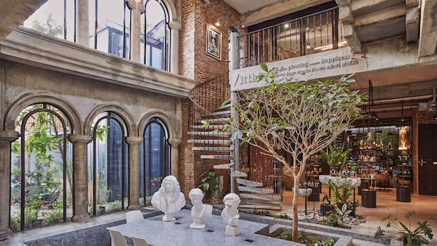 A spacious indoor area with a central table surrounded by chairs, a staircase, and a variety of plants. - Cataleya Estate Boutique Hotel (Bangkok)
