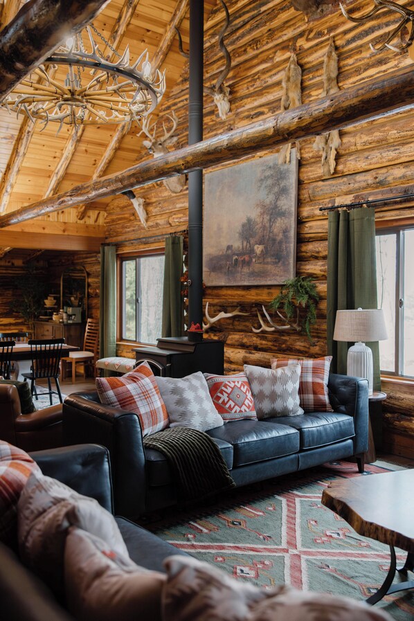 A rustic cabin interior with a leather sofa, a dining area, and a large painting on the wall.