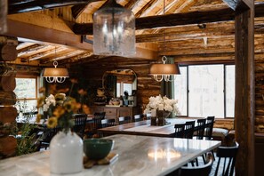 A rustic wooden interior with a large dining table, chairs, and hanging pendant lights.