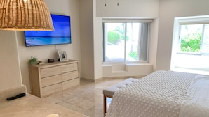 Un dormitorio con cama, televisor, cómoda, ventana y bandeja con velas.