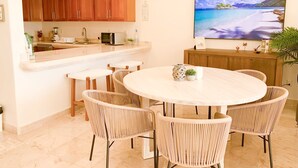 Una cocina moderna con armarios de madera, una encimera blanca y una zona de comedor con sillas de mimbre y una mesa redonda.