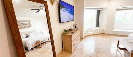 Un dormitorio con un espejo grande, una cama, un aparador, un televisor y un ventilador de techo.