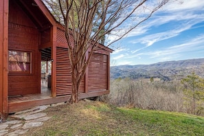 Una baita di legno con veranda, vista sulle montagne e un albero di fronte.