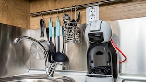 A modern kitchen with a stainless steel sink, a coffee maker, and utensils hanging on a rack.