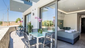 A modern hotel room with a glass door leading to a balcony, a bed with a grey mattress, and a small table with chairs.