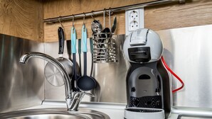 Une cuisine moderne dotée d’un évier en acier inoxydable, d’une machine à café et d’ustensiles de cuisine suspendus à un porte-ustensiles.