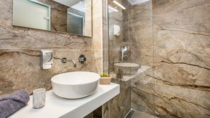 Une salle de bain moderne avec un lavabo en marbre, une cabine de douche en verre et un mur recouvert de carreaux de marbre.