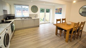 Una cocina moderna con lavadora integrada, un comedor con mesa y sillas de madera, y un reloj de pared grande.