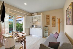 A compact living space with a kitchenette, a dining area, a sofa, and a view through a sliding door to an outdoor area.