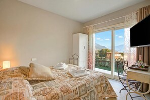 A hotel room with a bed, a desk, a chair, a TV, and a balcony with a view.