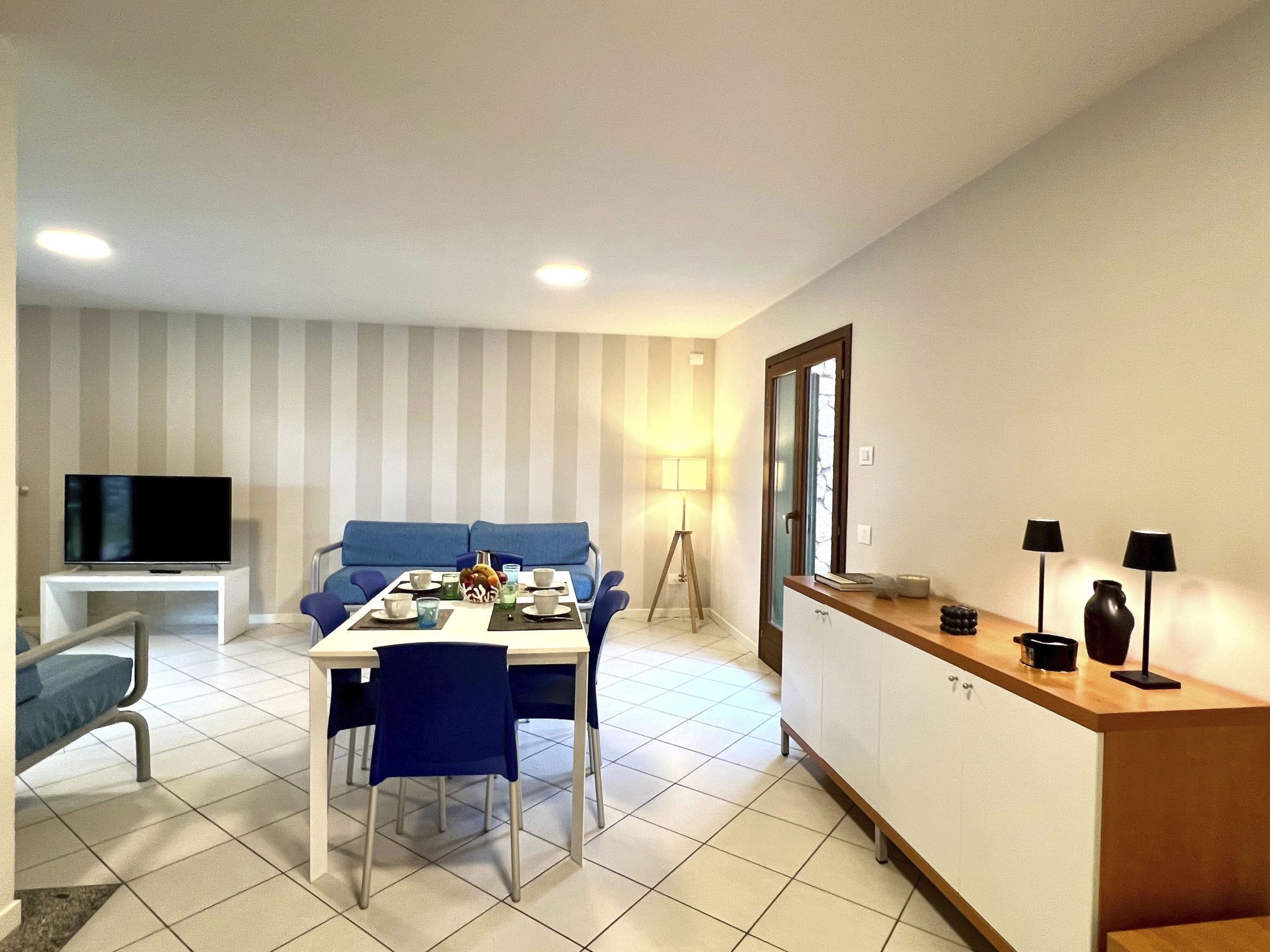 A modern living room with a dining area, a sofa, a TV, and a lamp.