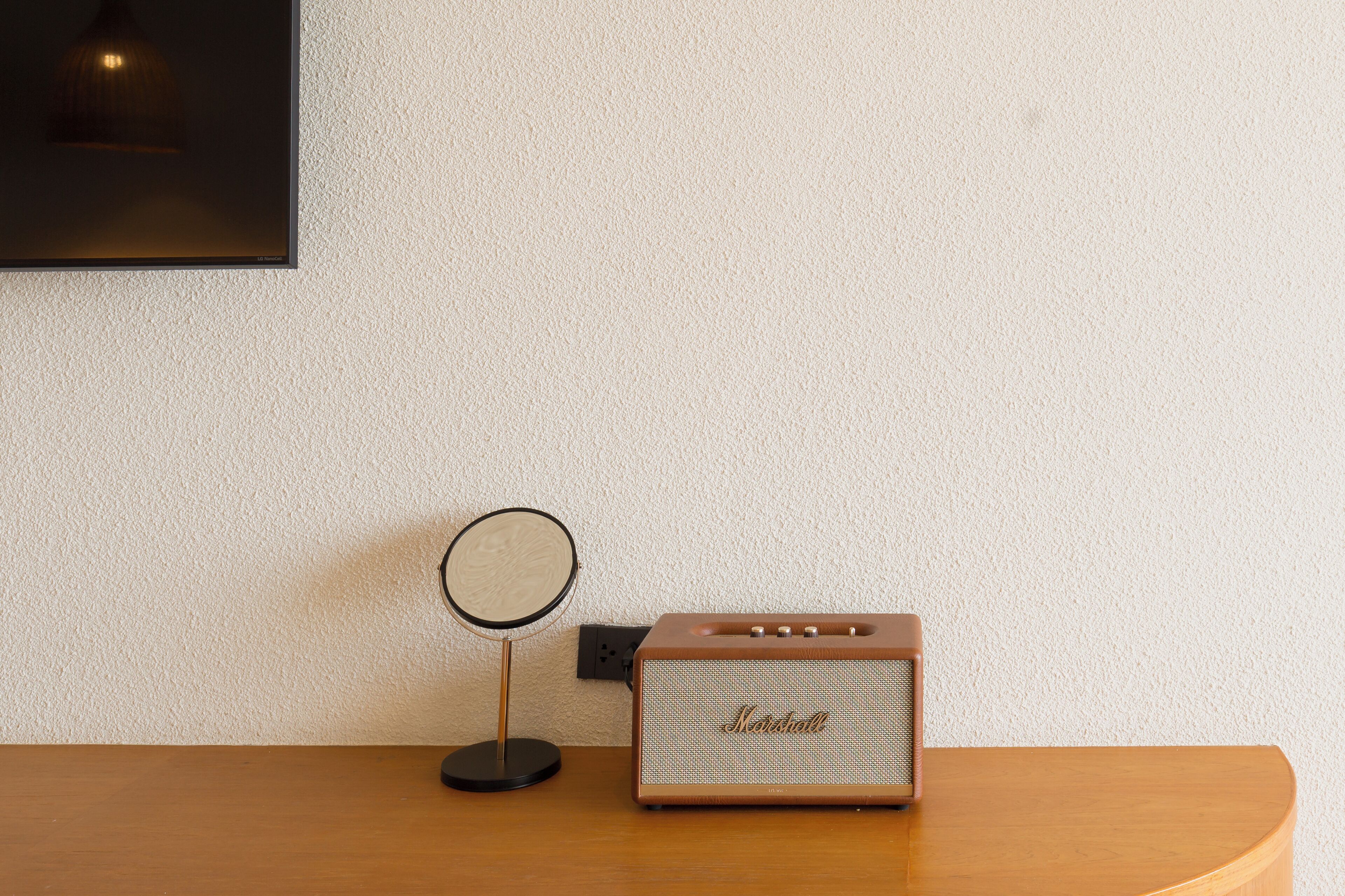A wooden table with a vintage Marshall speaker and a round mirror on a wall with a power outlet.