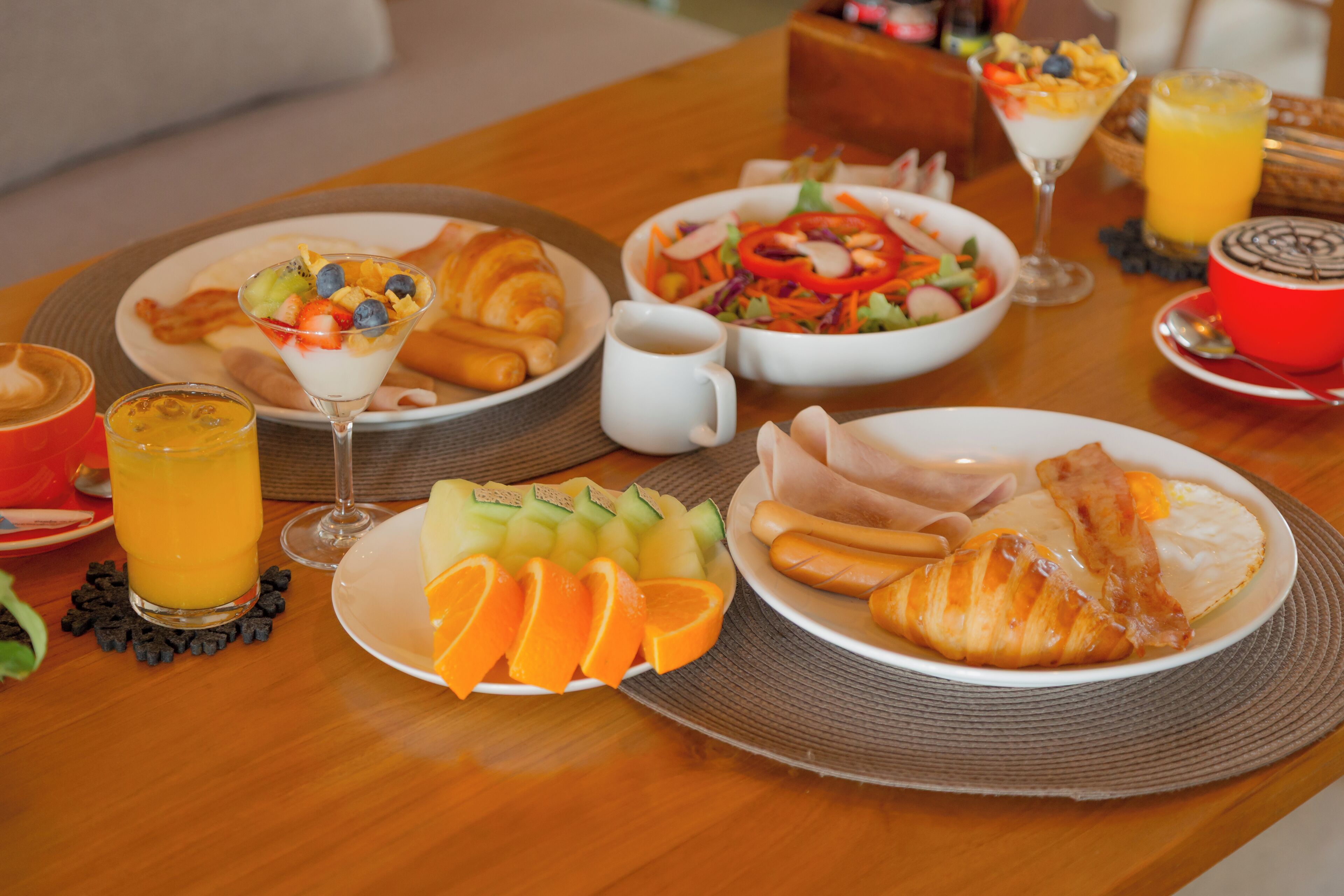 Ein Frühstückstisch mit Croissants, Obst, einem Salat und einem Glas Orangensaft.