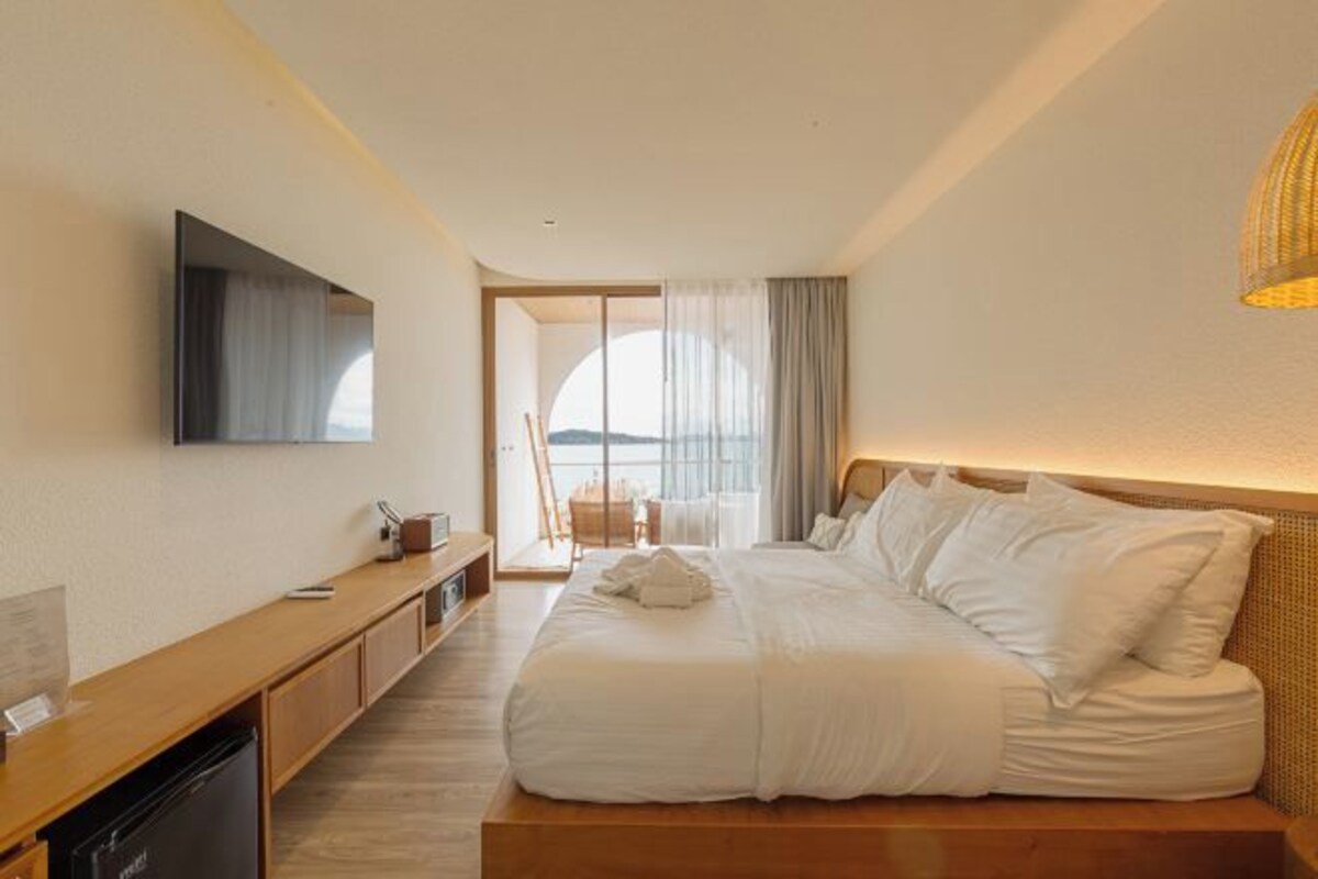 Habitación de hotel con una cama grande, un televisor de pantalla plana en la pared, un escritorio de madera con cafetera y vistas al exterior a través de un ventanal amplio.