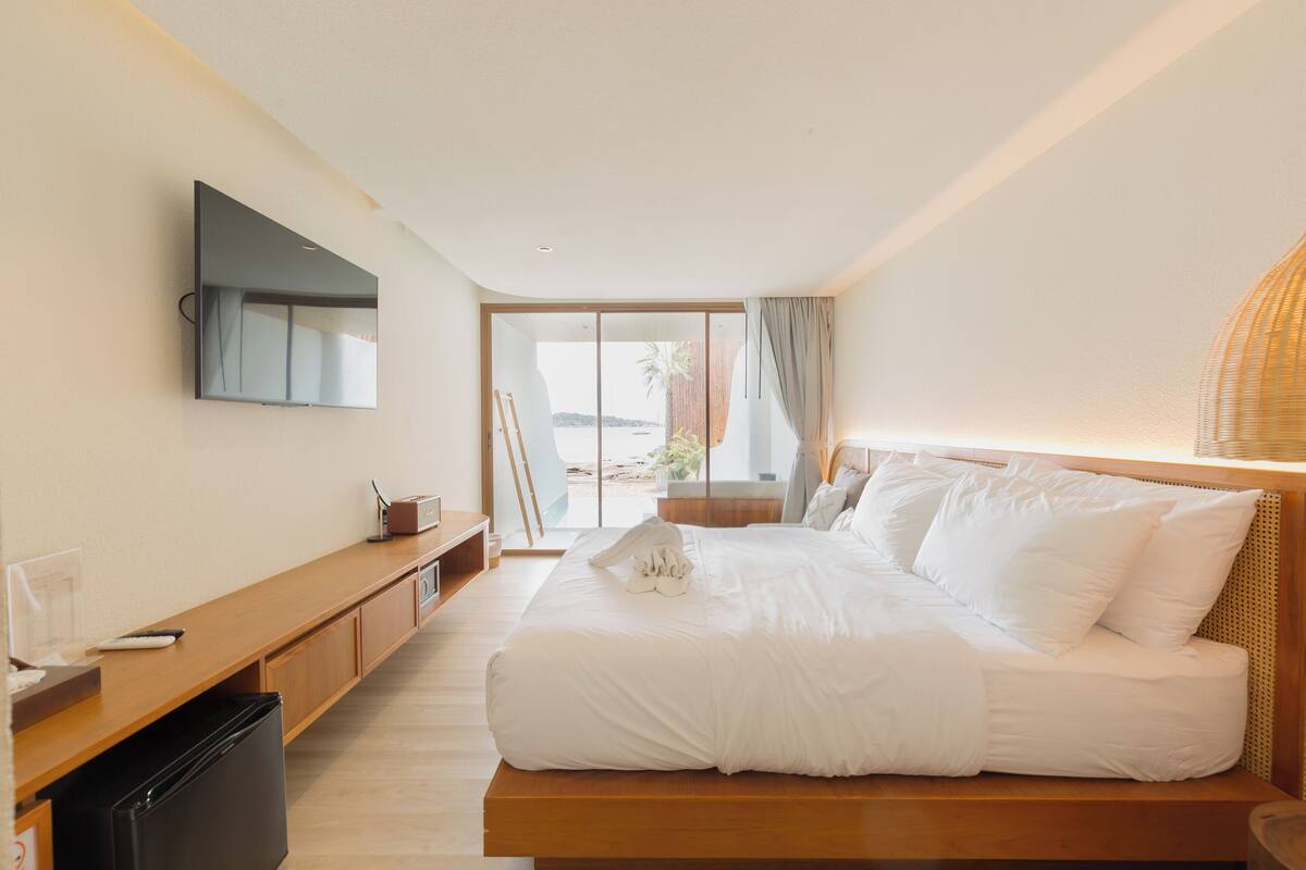 Ein modernes Hotelzimmer mit Bett, Wand-Fernseher, Schreibtisch aus Holz und Blick ins Freie.