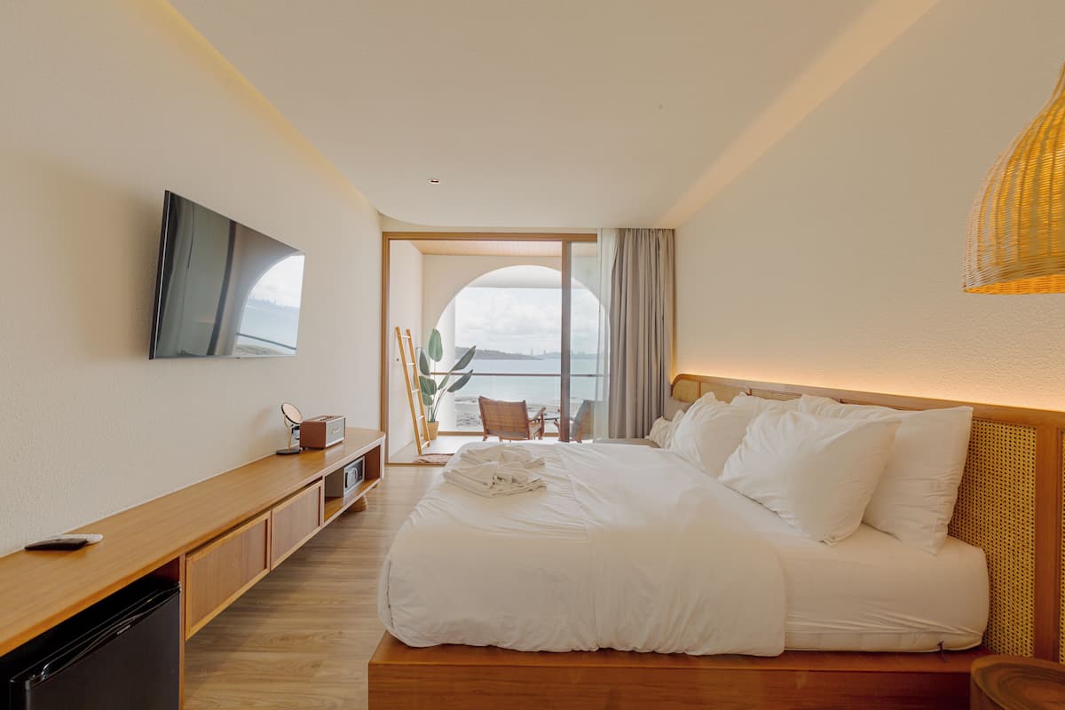 Ein modernes Hotelzimmer mit einem großen Bett, einem flachbildfernseher an der Wand, einem Holztisch und Meerblick durch ein großes Fenster.