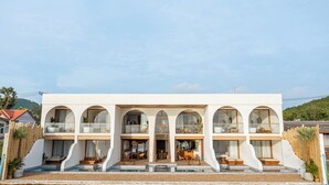 Un edificio moderno de varios pisos con amplios ventanales arqueados, una zona de piscina y asientos al aire libre.