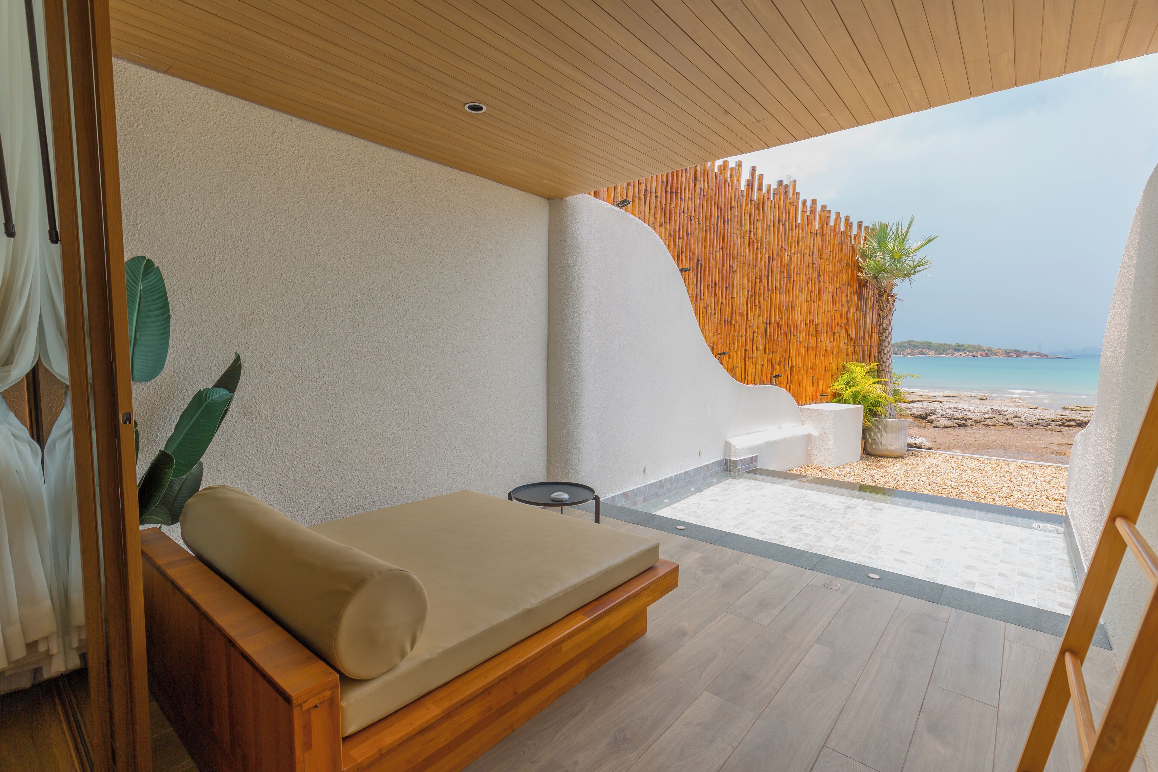 A modern room with a bed, a small table, and a view of the beach and sea.