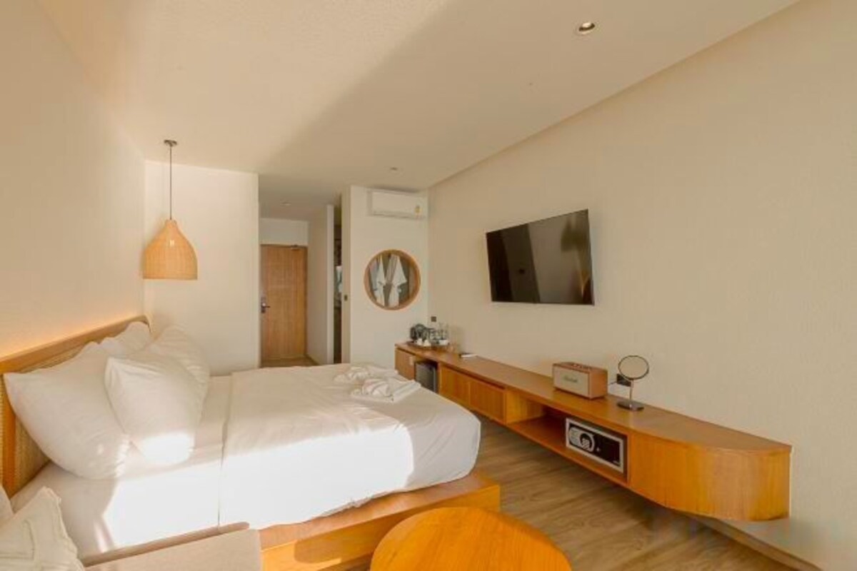 Una habitación de hotel moderna con cama, mesita de noche, televisor y un banco de madera.
