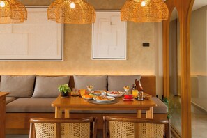Un comedor con mesa de madera dispuesta para el desayuno, un sofá, sillas de mimbre y lámparas decorativas tejidas.