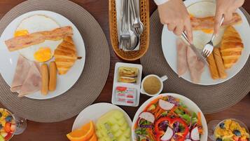 Un desayuno con platos de huevos, tocino y jamón, un tazón de fruta y una ensalada.