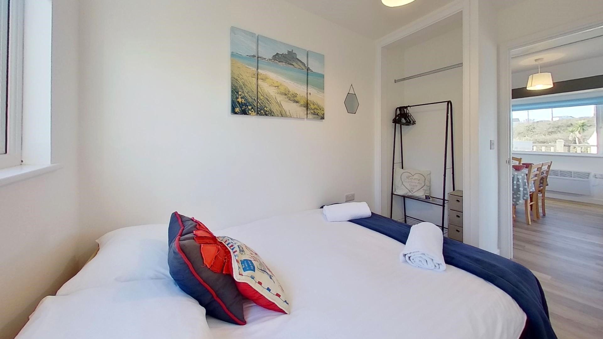 Ein Hotelzimmer mit Bett, einem Strandbild, einem Spiegel und Blick auf einen Balkon mit Gartenmöbeln.