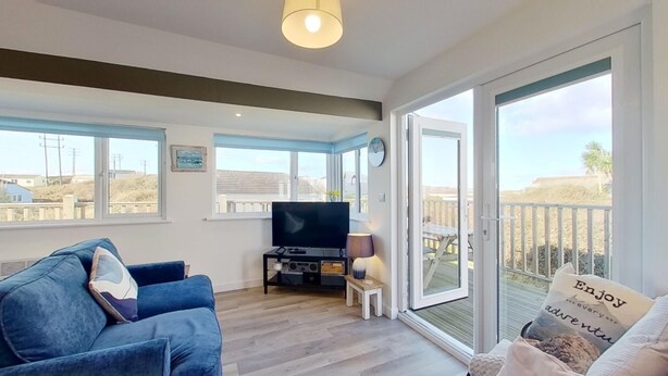 A living room with a blue sofa, a TV, and a sliding glass door leading to an outdoor deck.