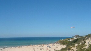 A beach with a sandy shore, a clear blue sky, and a person paragliding in the distance.