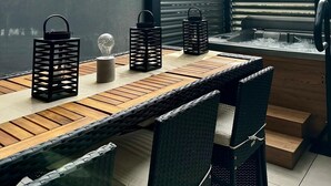 Un espace repas extérieur moderne, avec une table et des chaises en bois, des lanternes noires et une vue sur l’extérieur grâce à un plafond à lattes.