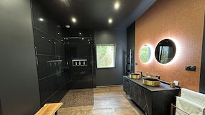 Une salle de bain moderne avec un meuble-lavabo noir, un miroir rond et un banc.