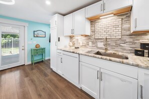 Uma cozinha com armários brancos, bancada de mármore e painel de azulejos.