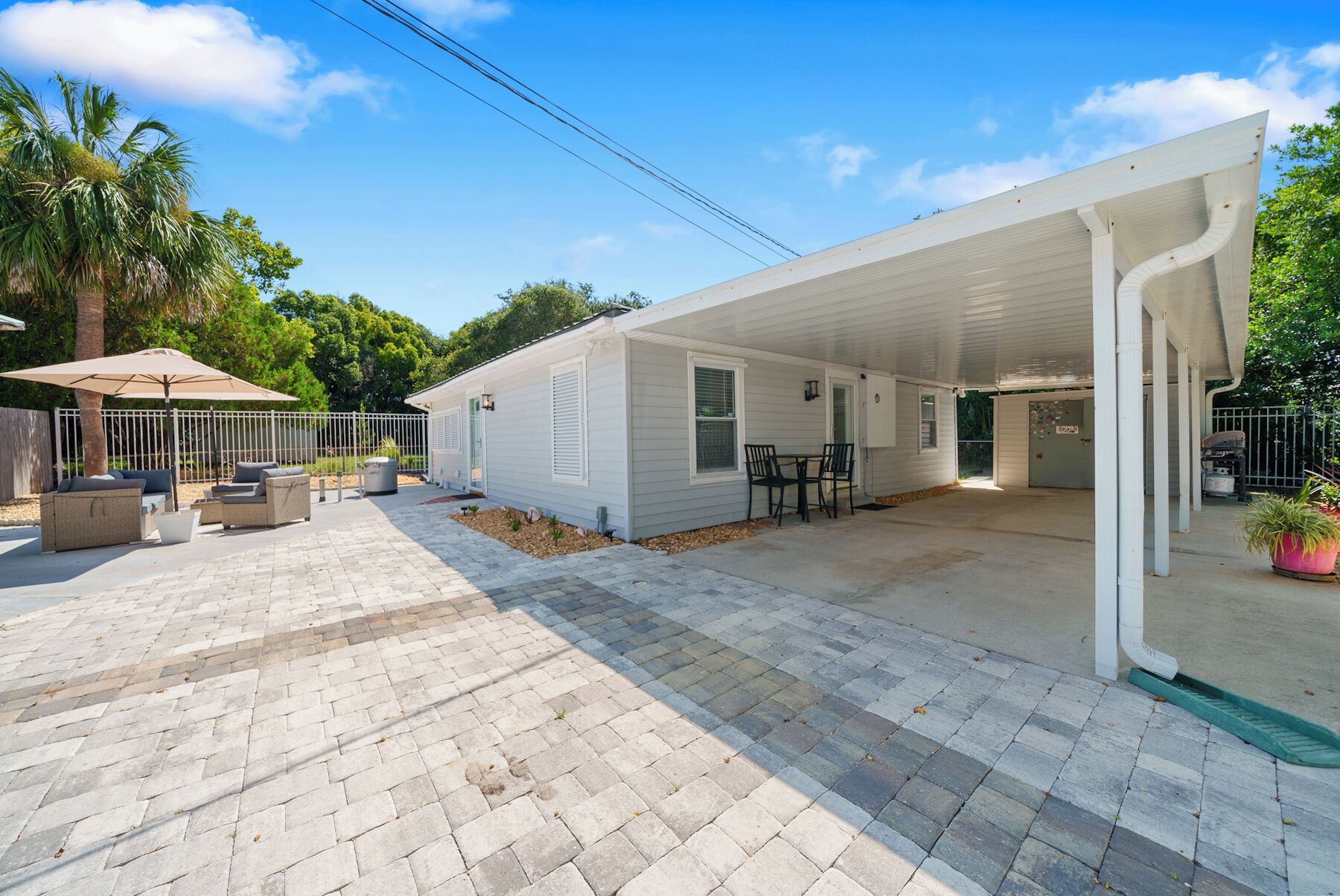 Ein Bungalow mit überdachter Terrasse, Sitzgelegenheiten im Freien und einem eingezäunten Garten.