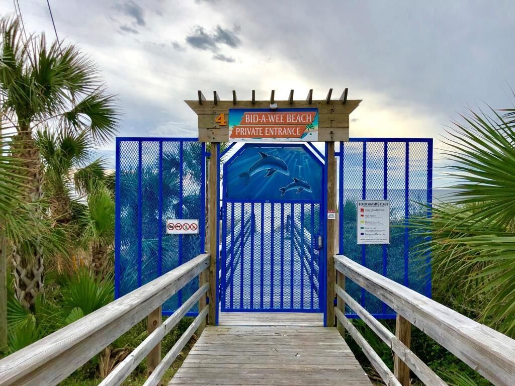 A wooden boardwalk leading to a blue gate with a sign indicating a private entrance to Bid-A-Wee Beach.