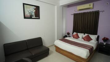 A bedroom with a bed, a dark sofa, a nightstand, an air conditioner, and a framed painting on the wall.