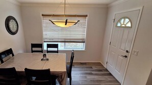 Un comedor con una mesa, sillas, un reloj y una ventana con persianas.