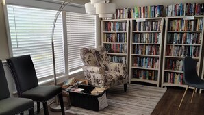 Een woonkamer met een bank, twee fauteuils, een salontafel, een vloerlamp en een boekenplank vol boeken.