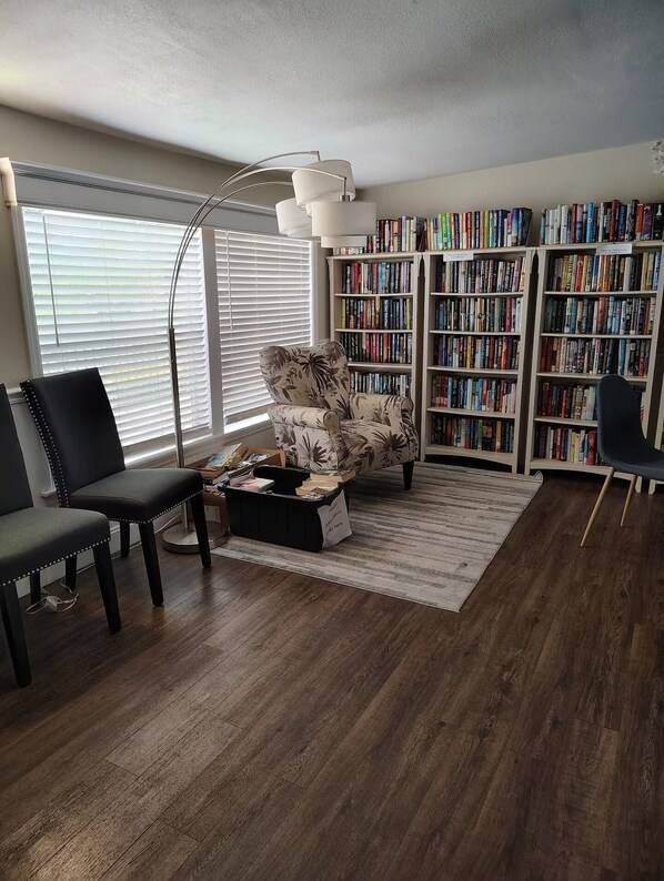 A living room with a sofa, two chairs, a coffee table, a floor lamp, and a bookshelf filled with books.