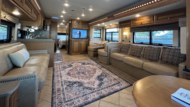 Goed verlicht interieur van een camper, met een keuken, een zithoek met een groot vloerkleed, en een televisie.
