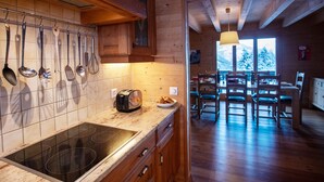 A wooden cabin kitchen with a built-in stove, hanging utensils, and a dining area with wooden chairs and a table.