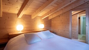 A wooden cabin bedroom with a bed, two wall-mounted lights, and a glass door leading to a bathroom.