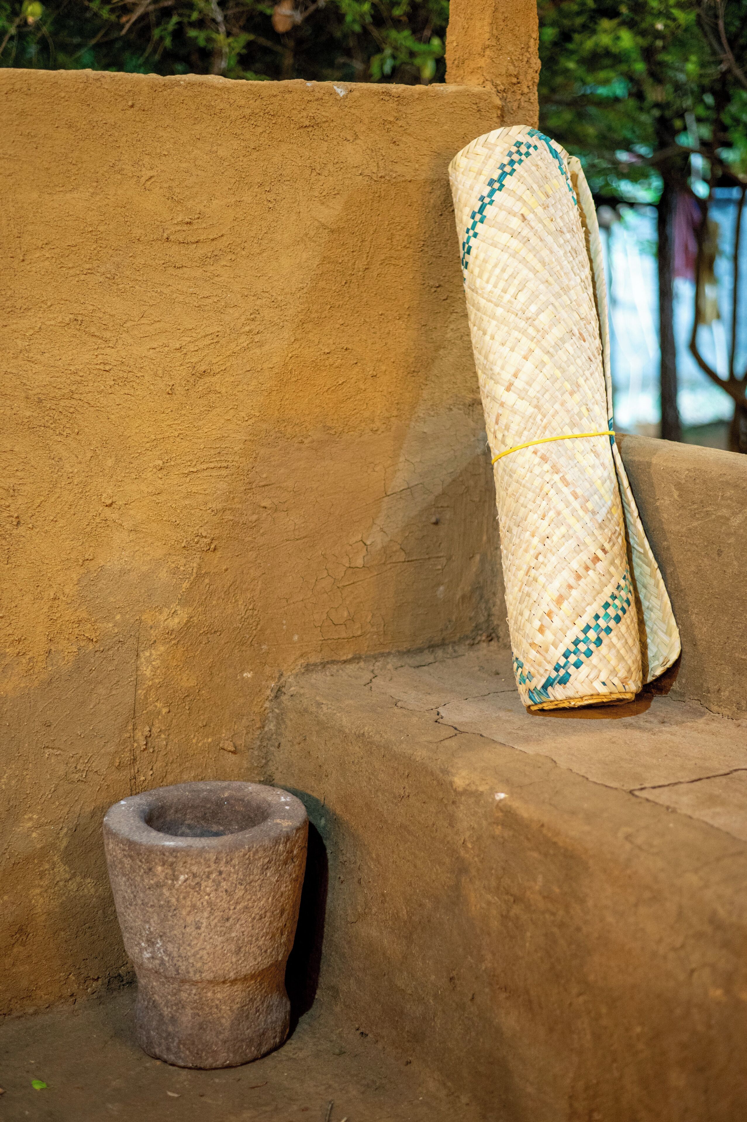 A stone mortar and a woven mat leaning against a wall.