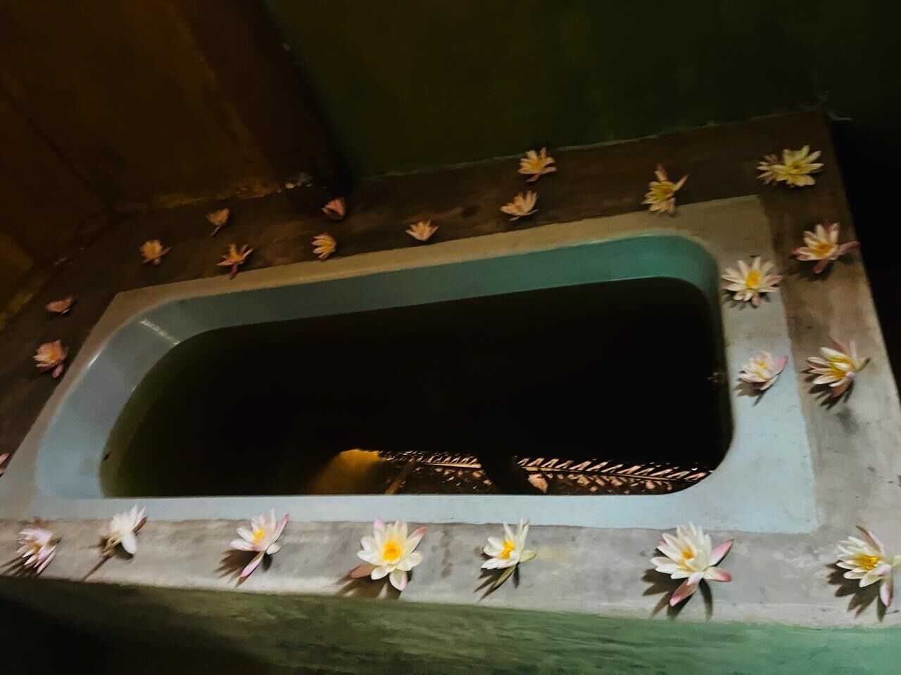 Una bañera rectangular con el interior oscuro, rodeada por un borde decorado con nenúfares artificiales.